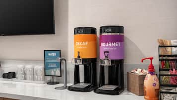 Una estación de dispensador de agua con dos dispensadores de bebidas, uno etiquetado 'DECAF' y otro 'GOURMET', una cafetera y una estación de café con un dispensador de leche.