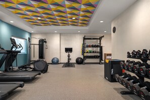 Un gimnasio con cintas de correr, bicicletas estáticas, una máquina de remo y una variedad de pesas y pelotas de ejercicio.