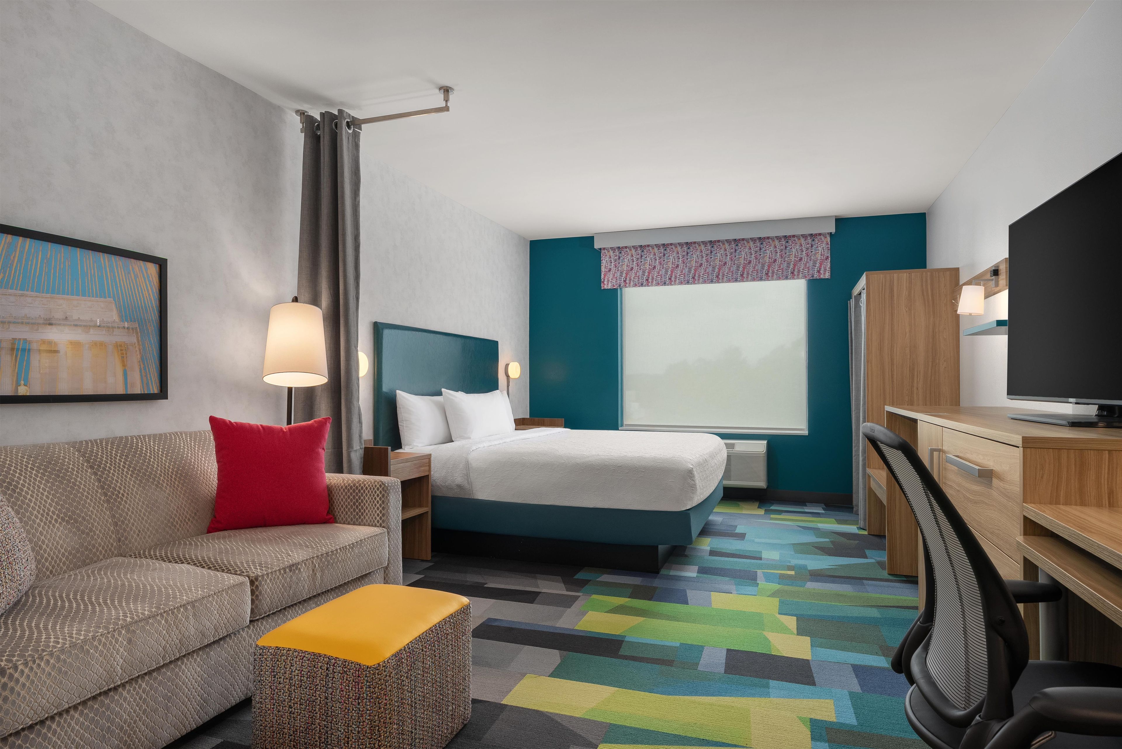 A hotel room with a bed, a desk, a television, a sofa, and a colorful carpet.