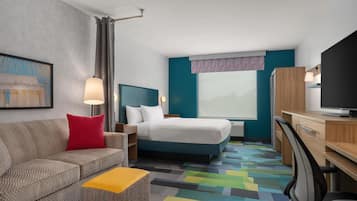 A hotel room with a bed, a desk, a television, a sofa, and a colorful carpet.