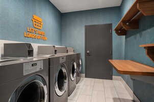 Un moderno lavadero con una pared estampada con un patrón de espiga azul, un letrero que dice 'LET'S HAVE LOADS OF FUN' y una puerta con un estante de madera encima.