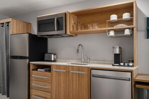 Cocina compacta con refrigerador, microondas, tostadora, pileta y alacenas de madera.