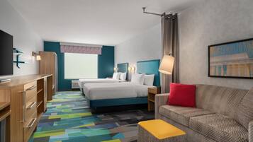 Quarto de hotel com cama, sofá, televisão, escrivaninha e tapete colorido.