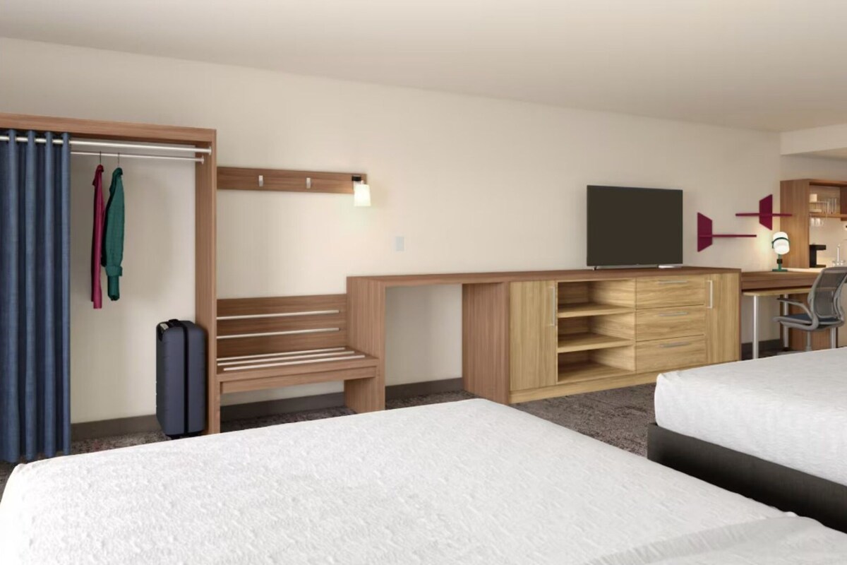 Een hotelkamer met twee bedden, een bureau met een televisie, een kledingkast en een zithoek met een bankje en een stoel.