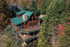 A cabin with a green roof, wooden exterior, and a deck with outdoor seating. - Highland View (Sevierville)