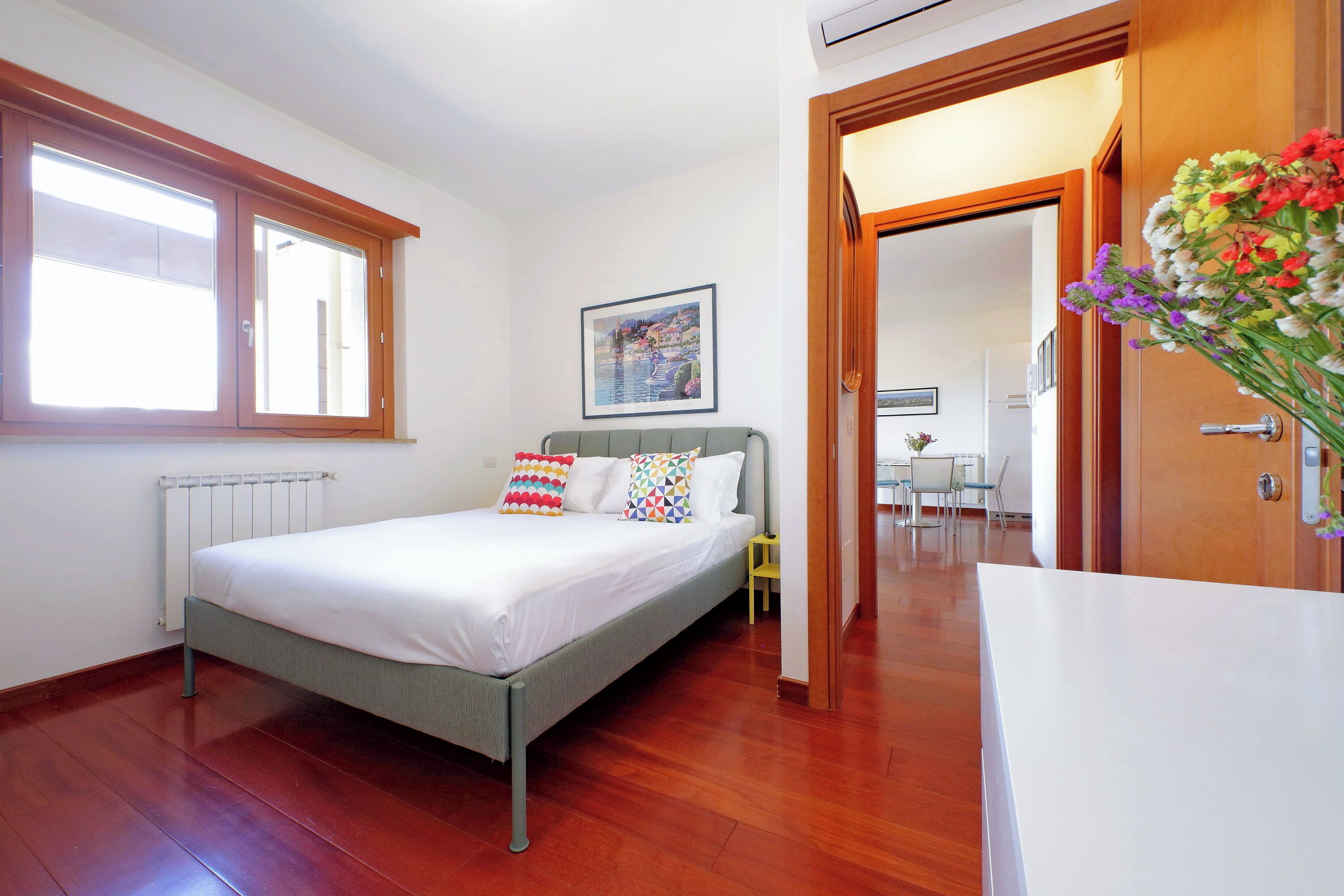 A bedroom with a bed, a radiator, a window, a door, and a picture on the wall.
