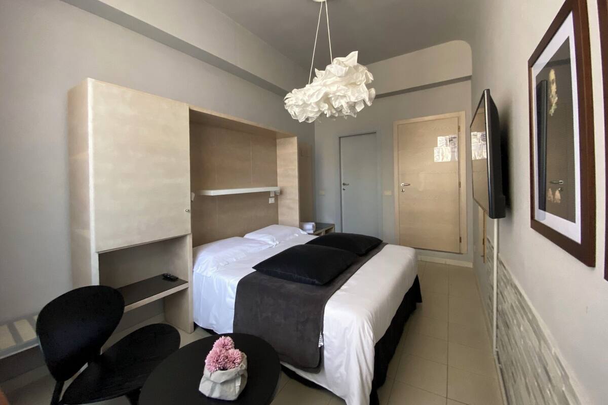 Una habitación de hotel con cama, escritorio, silla, televisor y una lámpara en el techo.