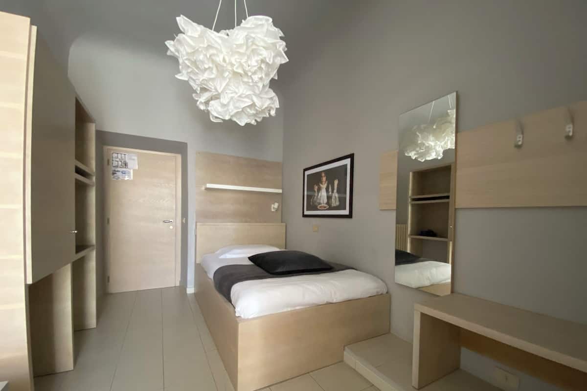 Un dormitorio moderno con cama, mesitas de noche, lámpara colgante, espejo y estanterías integradas.