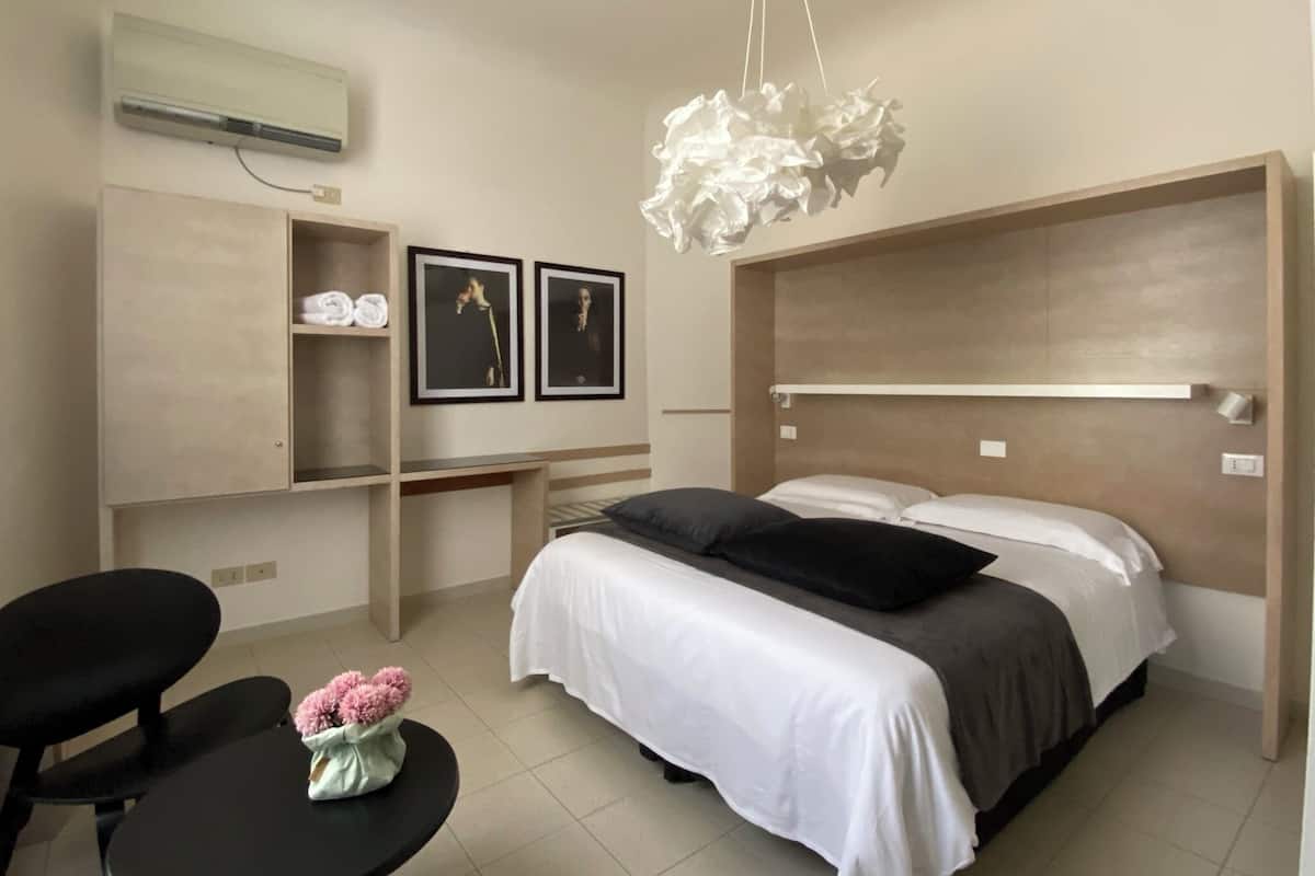 Una habitación de hotel moderna con una cama, un escritorio y una silla. Hay una pequeña mesa con un jarrón de flores.