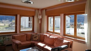 A cozy living room with a sectional sofa, a glass coffee table, and large windows offering a view of the outdoors. - Residenza San Giorgio, your home in the Belluno Dolomites National Park.  (Veneto)