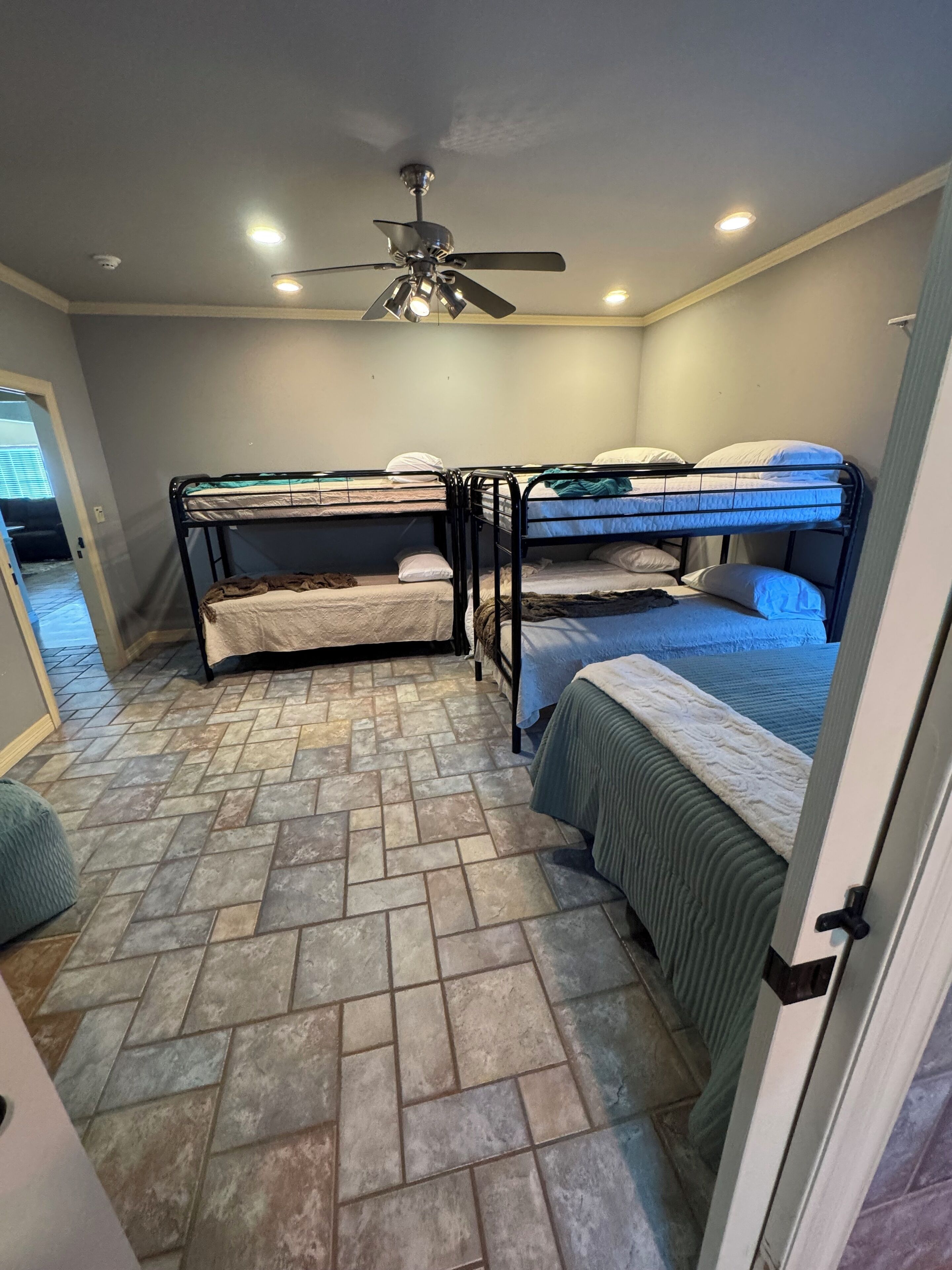 A room with three bunk beds, a ceiling fan, and a herringbone-patterned tiled floor.