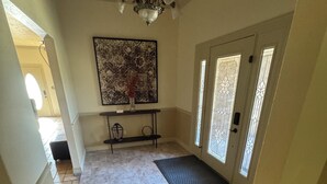 Ein geräumiges Foyer mit Marmorboden, einer schwarzen Fußmatte am Eingang, einer Kandelaberleuchtre und einem großen, abstrakten Gemälde an der Wand.