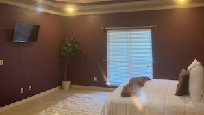 Ein Schlafzimmer mit Bett, einer Topfpflanze, einem Fenster mit Jalousien und einer Deckenleuchte.