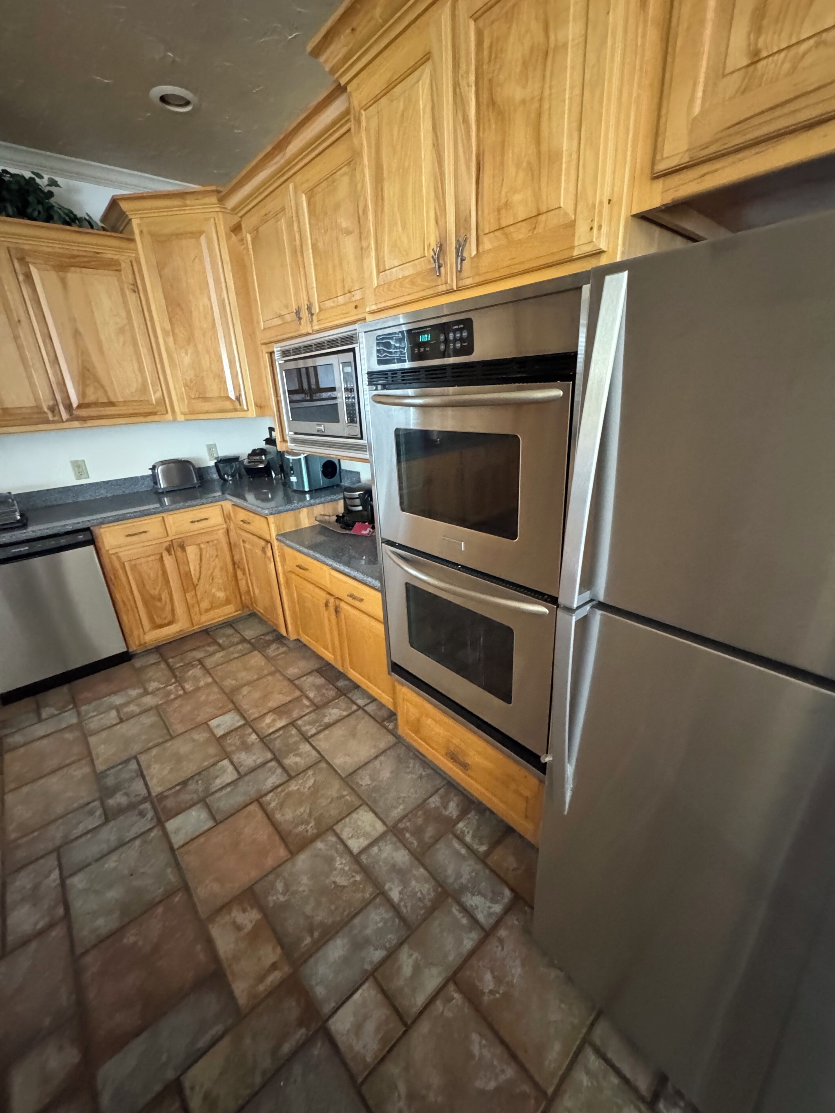 A kitchen with wooden cabinets, a stainless steel refrigerator, a microwave, and a double oven.