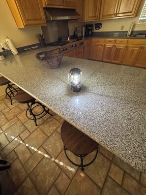 A kitchen with granite countertops, wooden cabinets, and a central island with bar stools.