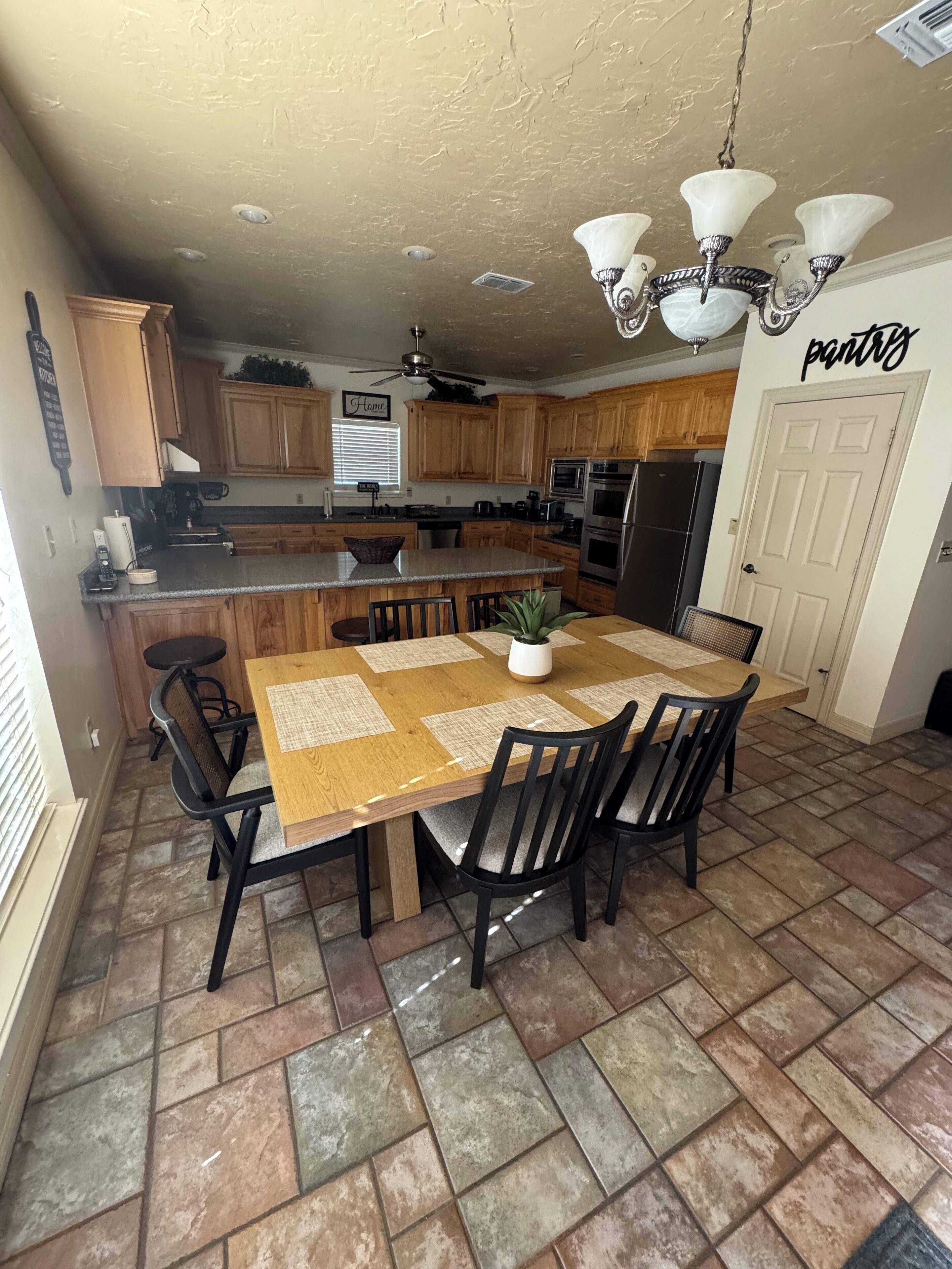 A kitchen with wooden cabinets, a central island, a dining table with chairs, and a chandelier.
