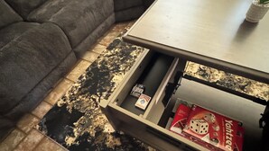 Ein Wohnzimmer mit einem dunkelgrauen Sofa, einem hellen Holztisch und einem gemusterten Teppich.