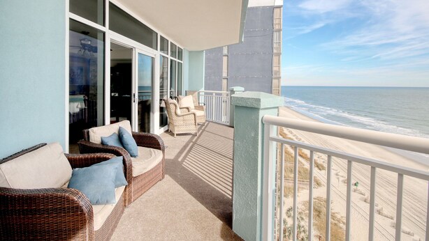Un balcon agrémenté de meubles en osier, une vue sur la plage et un bâtiment en arrière-plan.