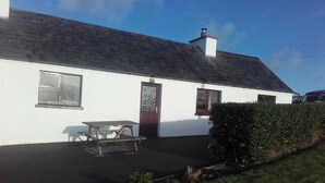 A white building with a dark roof, a door, and windows. There is a picnic table outside. - Atlantic Coast (Ballyganny)