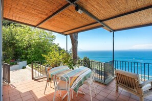 A covered patio with a table and chairs, overlooking a scenic view of the ocean. - Beautiful sea view with swimming pool (Massa Lubrense)