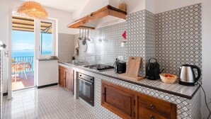 A kitchen with a large island, wooden cabinets, a hanging pot rack, and a view to a balcony. - Beautiful sea view with swimming pool (Massa Lubrense)
