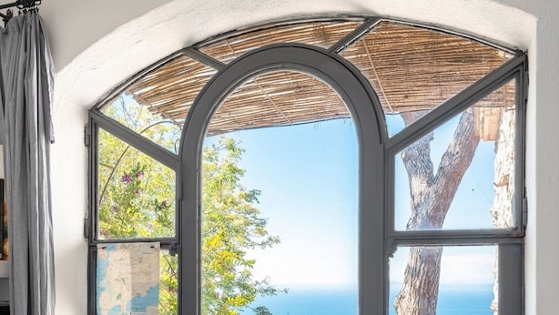 A room with a large arched window overlooking a patio with outdoor furniture and a view of the sea. - Beautiful sea view with swimming pool (Massa Lubrense)