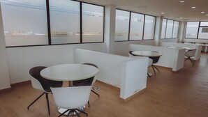 Een moderne kantoorruimte met ronde tafels en witte stoelen, grote ramen en een houten vloer.