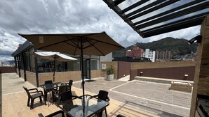 Een terras op het dak met buitenmeubilair, een pergola en uitzicht op een stadsbeeld en bergen.