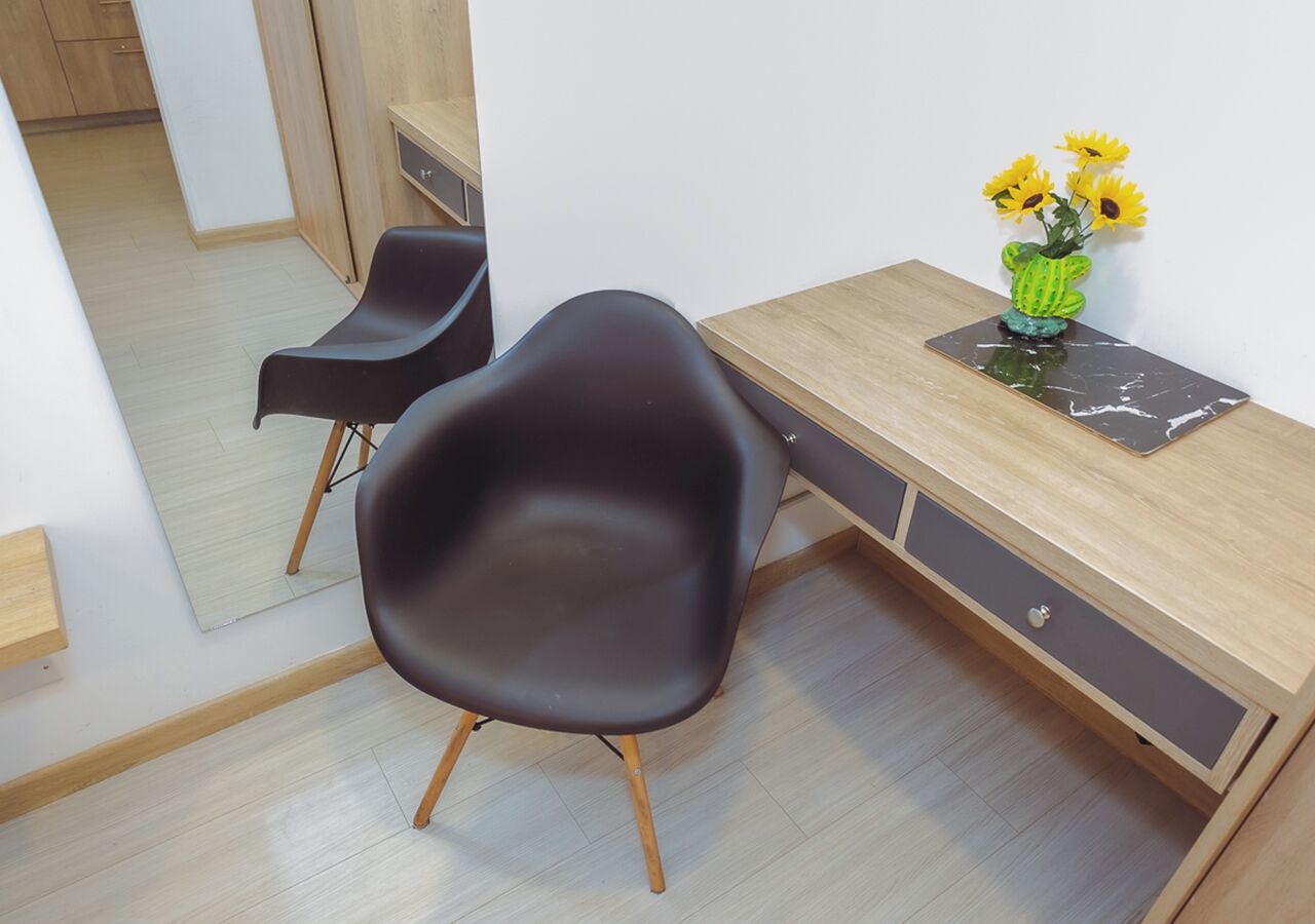 A modern room with a wooden desk, two black chairs, a mirror, and a vase with yellow flowers.