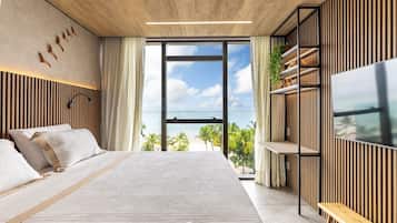 A modern bedroom with a large bed, a TV, and a view of the beach.