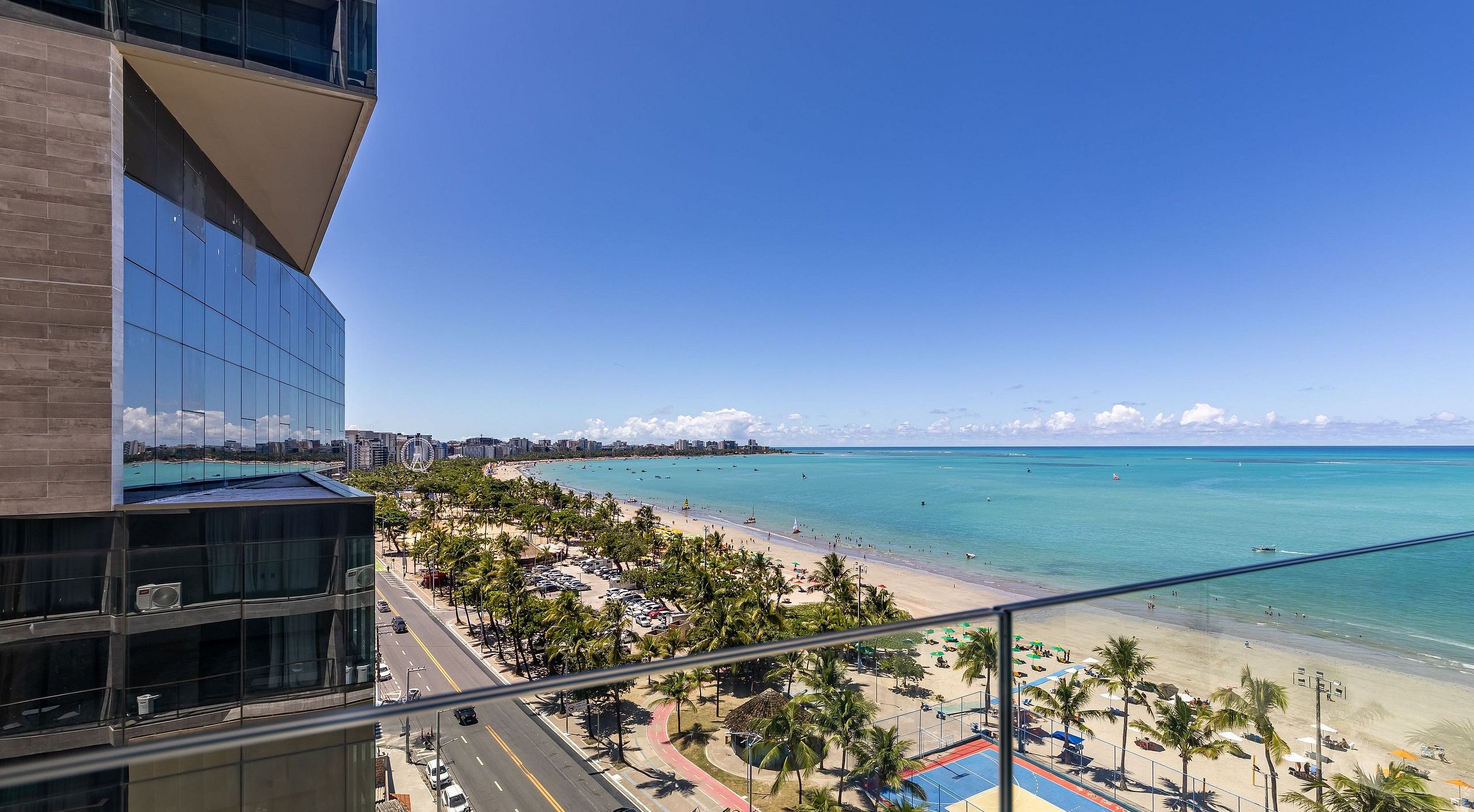 A beach view from a high-rise building with a clear sky, palm trees, and a distant cityscape.