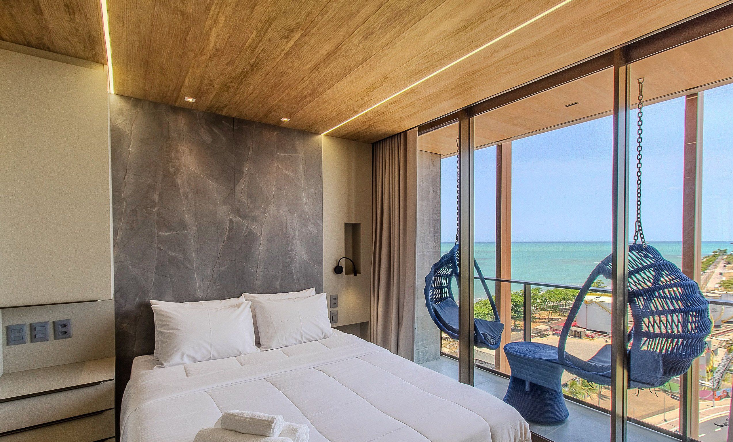 Ein modernes Schlafzimmer mit einem großen Bett, einer Marmorwand und Meerblick durch große Fenster.
