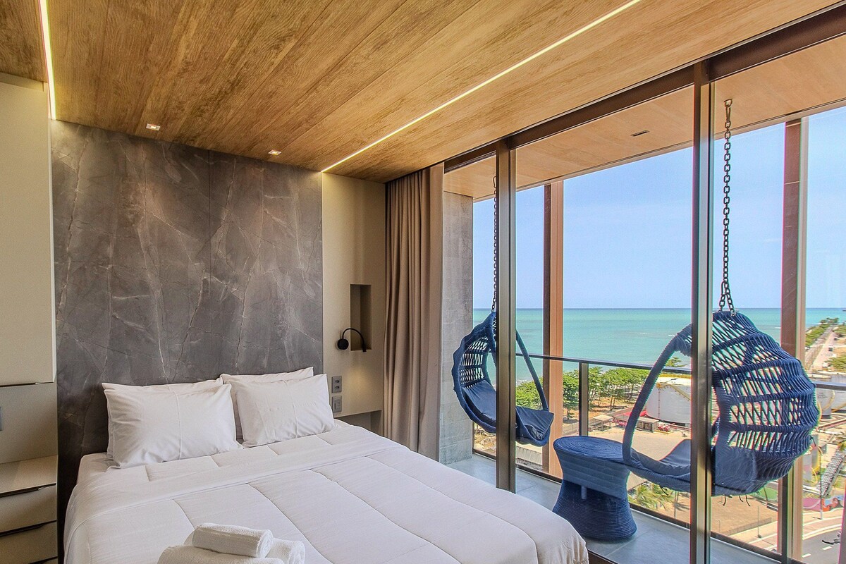 Une chambre moderne avec un grand lit, un mur en marbre et un balcon offrant une vue sur la mer.