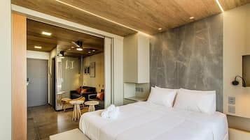 A modern hotel room with a large bed, a seating area with a sofa and chairs, and a bathroom visible through an open door.