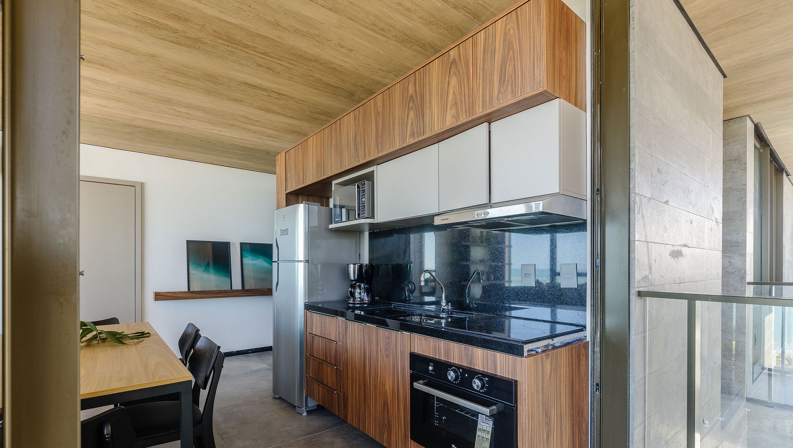 Una cocina moderna con armarios de madera, encimera negra y electrodomésticos de acero inoxidable.