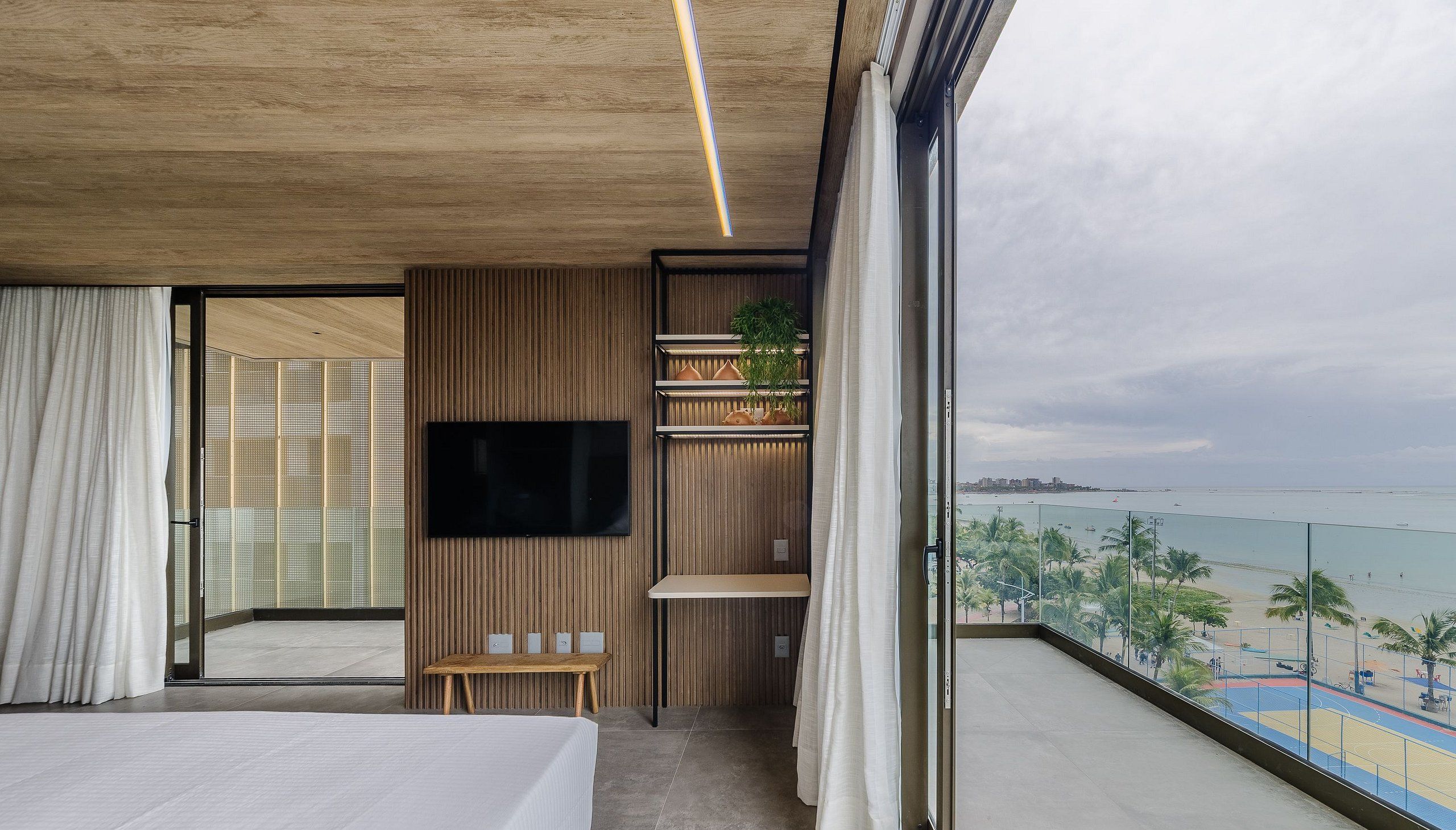 A modern hotel room with a large balcony, a flat-screen TV, and a view of the beach.
