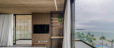 A modern hotel room with a large balcony, a flat-screen TV, and a view of the beach.