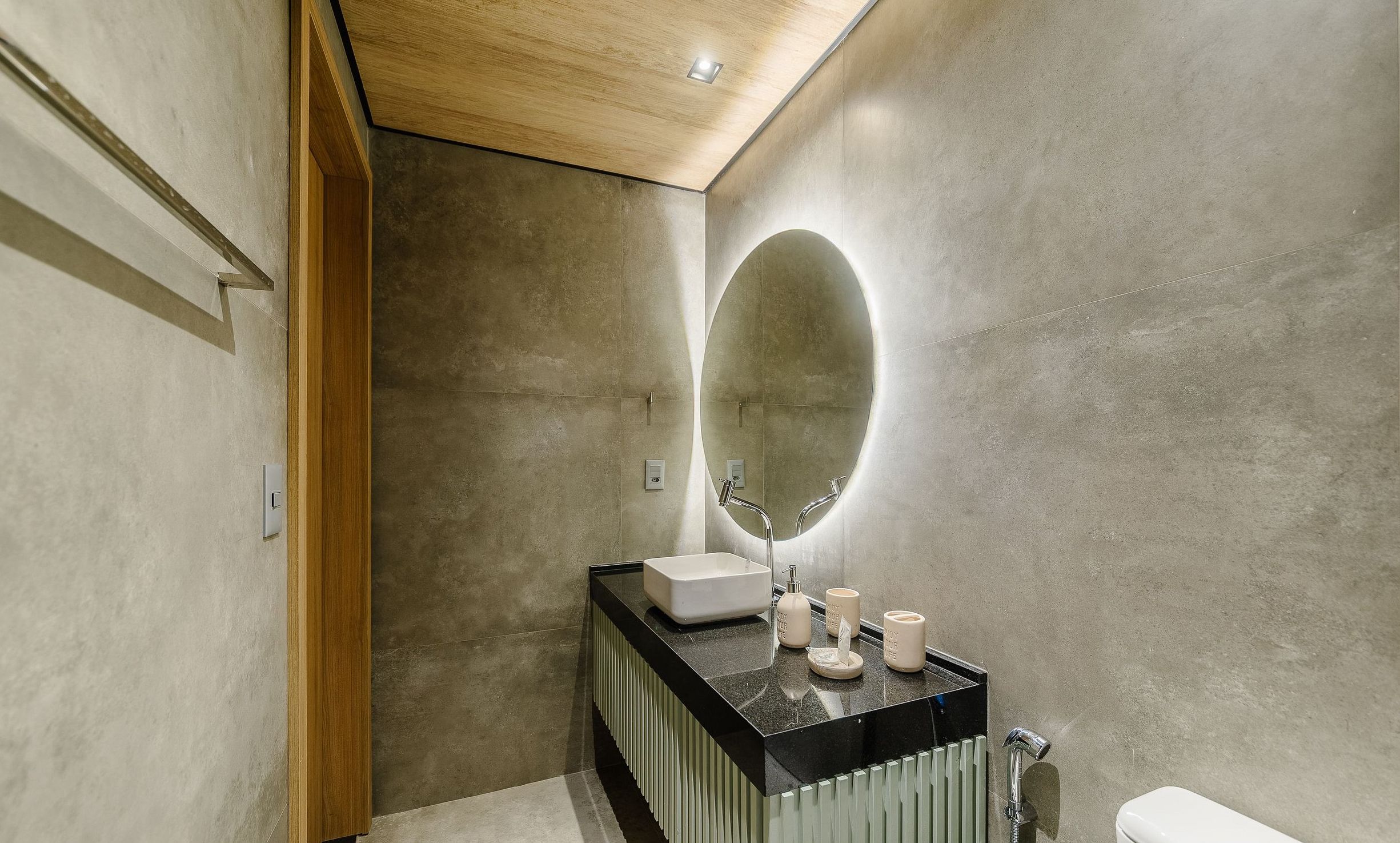 A modern bathroom with a large oval mirror, a black countertop, and a white sink.