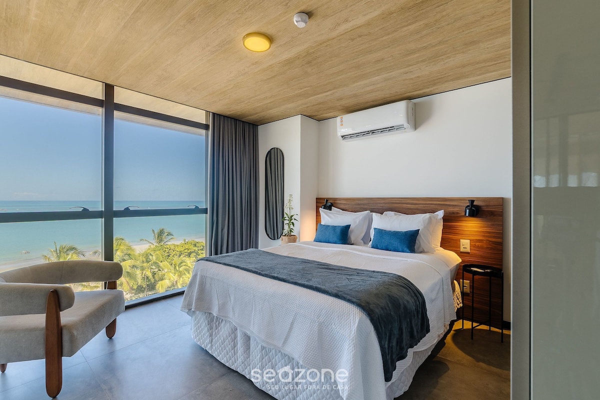 A modern bedroom with a large bed, a view of the ocean, and a wooden ceiling.