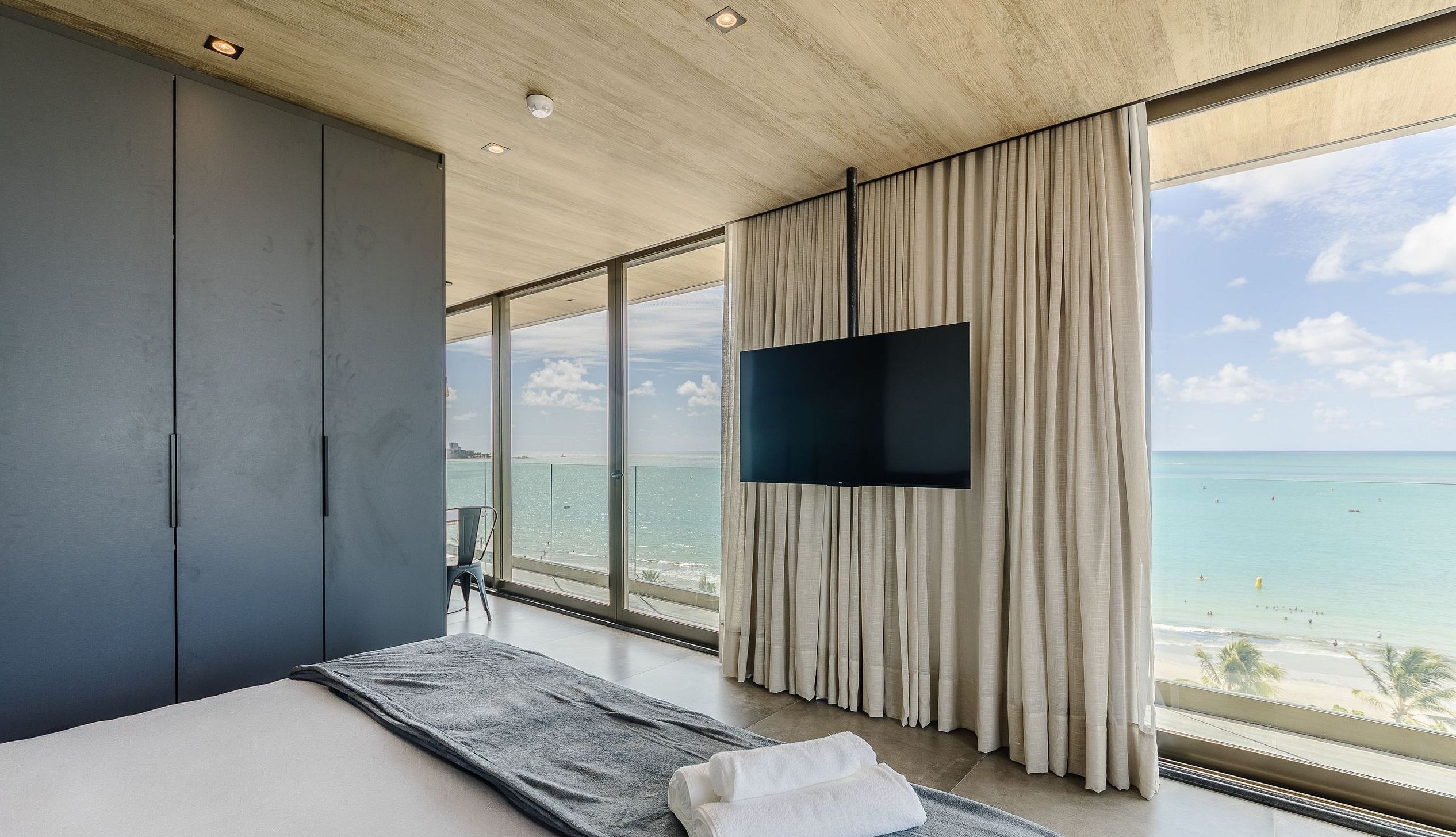 A modern hotel room with a large bed, a flat-screen TV, and a view of the ocean.