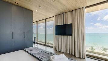 A modern hotel room with a large bed, a flat-screen TV, and a view of the ocean.