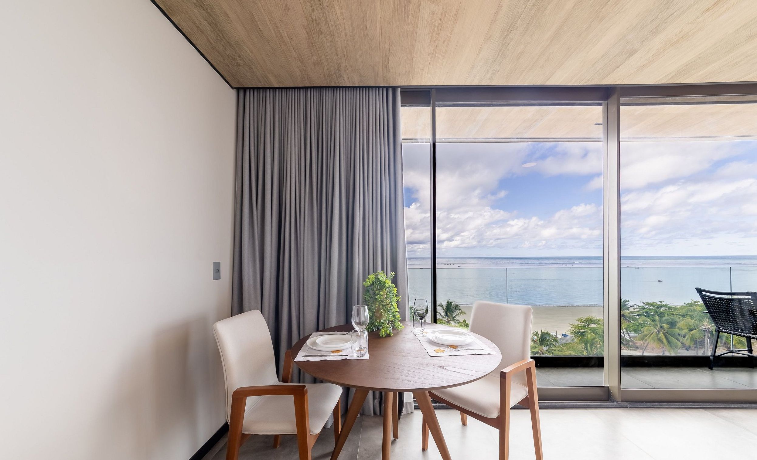 A modern dining area with a round table, two chairs, and a view of the sea through large windows.