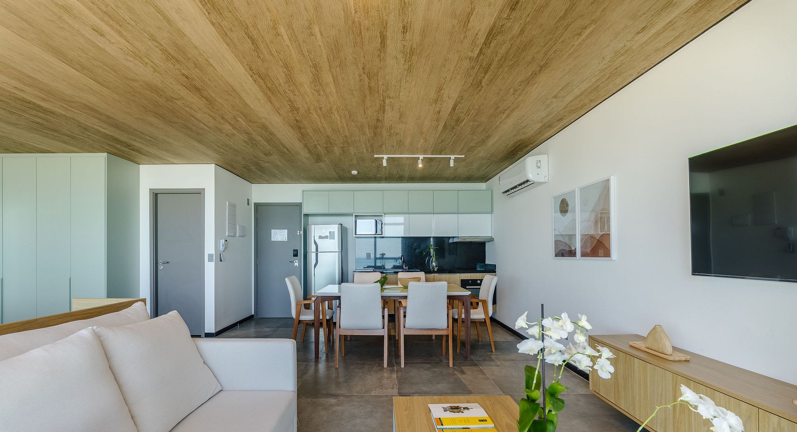 A modern living room with a sofa, dining area, kitchen, and a large TV.