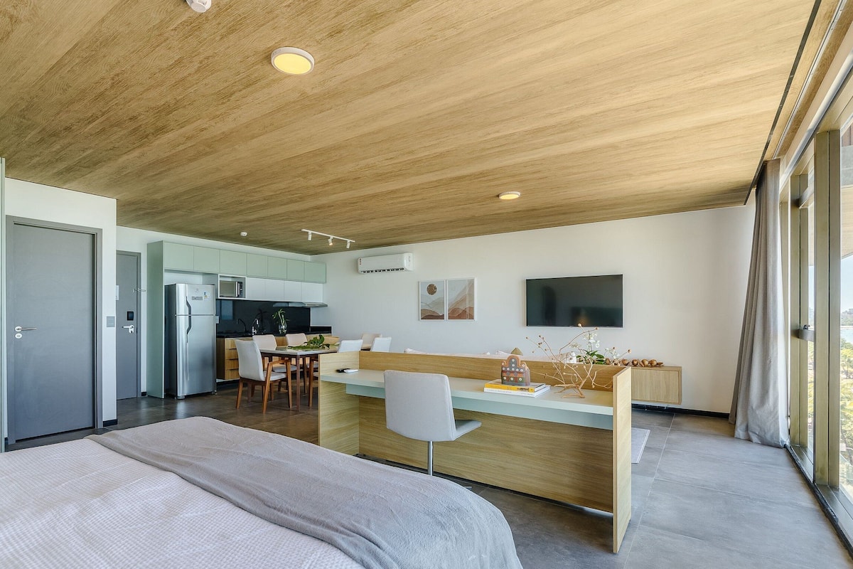 A modern kitchen with a central island, a dining area with a white table and chairs, and a large bed with a white blanket.