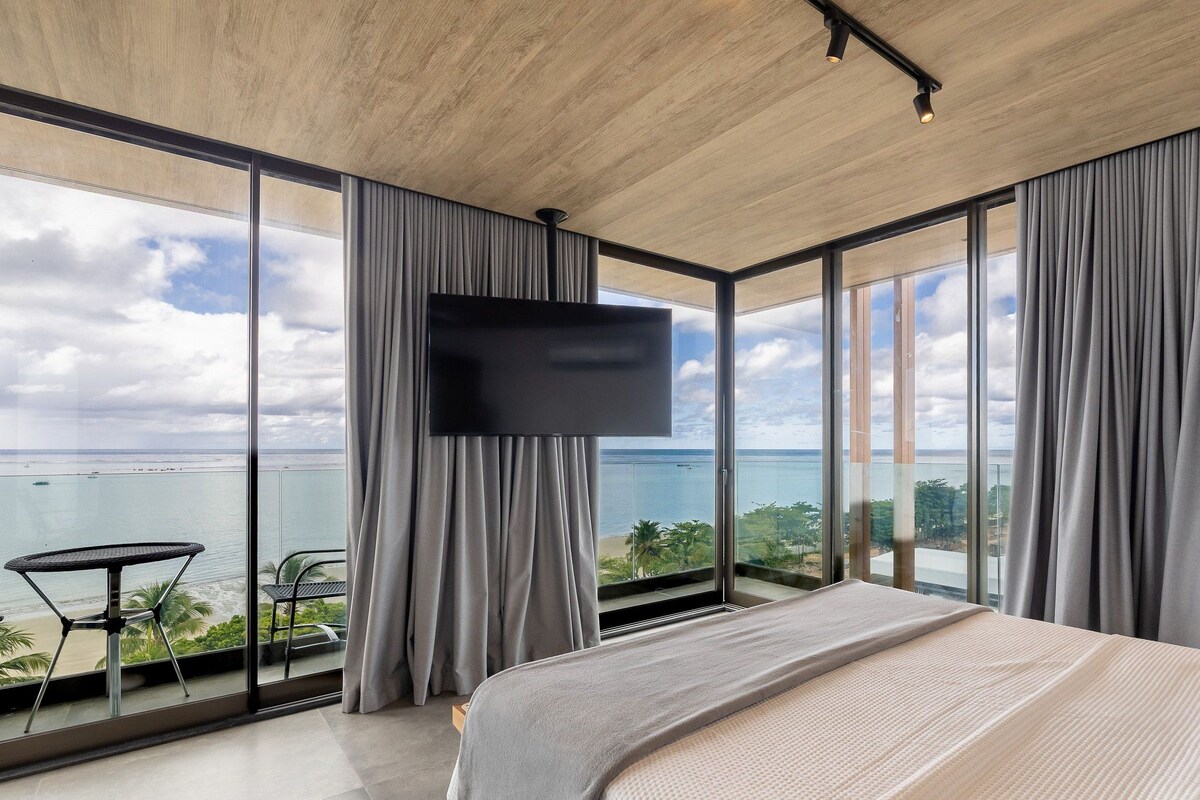 Une chambre moderne dotée d’un grand lit, d’un téléviseur à écran plat et d’un balcon offrant une vue sur la mer.