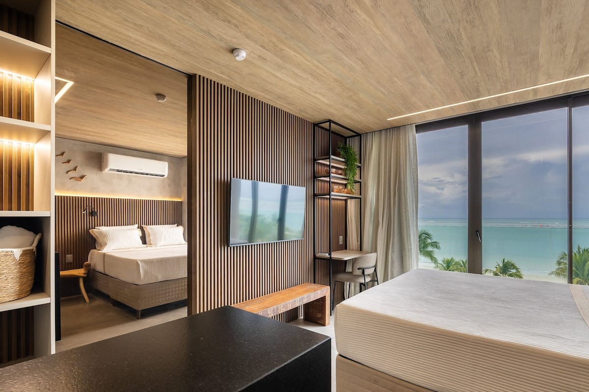 A modern hotel room with a large bed, a TV, a desk, and a balcony with a sea view.