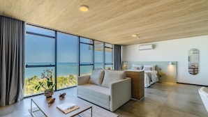 A modern hotel room with a large window offering a sea view, a sofa, a bedside table, and a small dining area. - NWTs - Apartamentos com Vista Frente-Mar (Maceió)