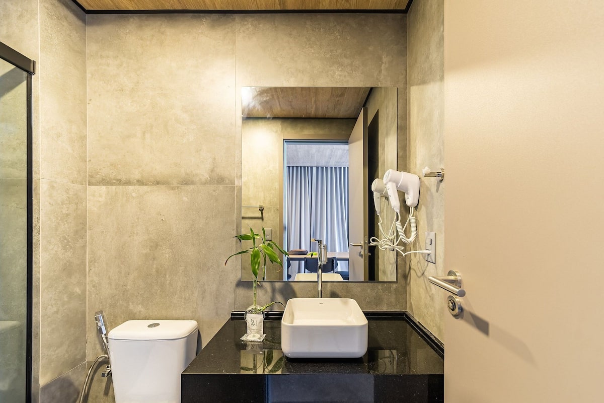 A modern bathroom with a large mirror, a sink, a toilet, and a hairdryer on the wall.