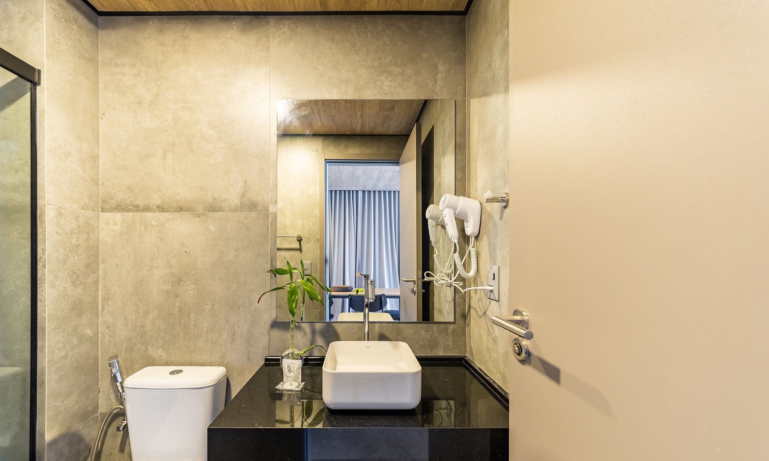 A modern bathroom with a large mirror, a sink, a toilet, and a hairdryer on the wall.