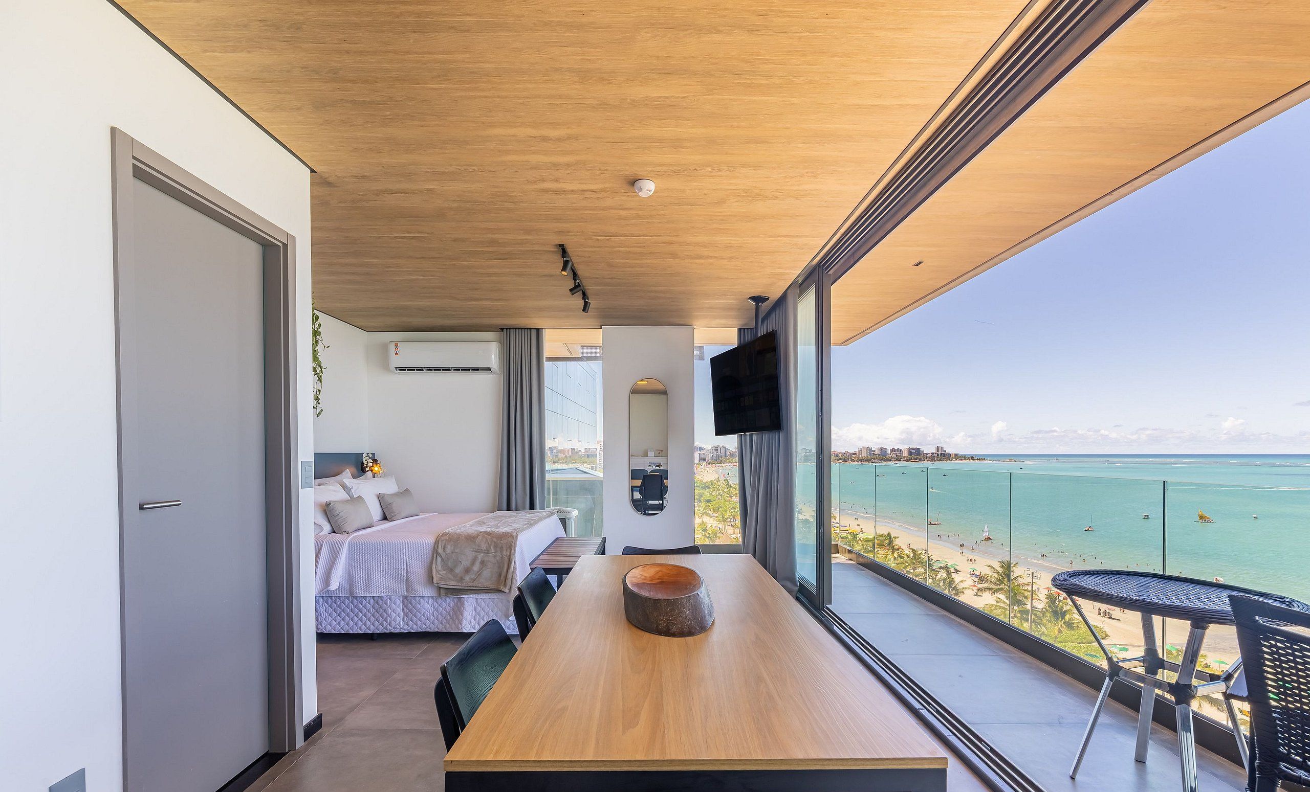 A modern bedroom with a bed, bedside table, and a large window overlooking a beach.